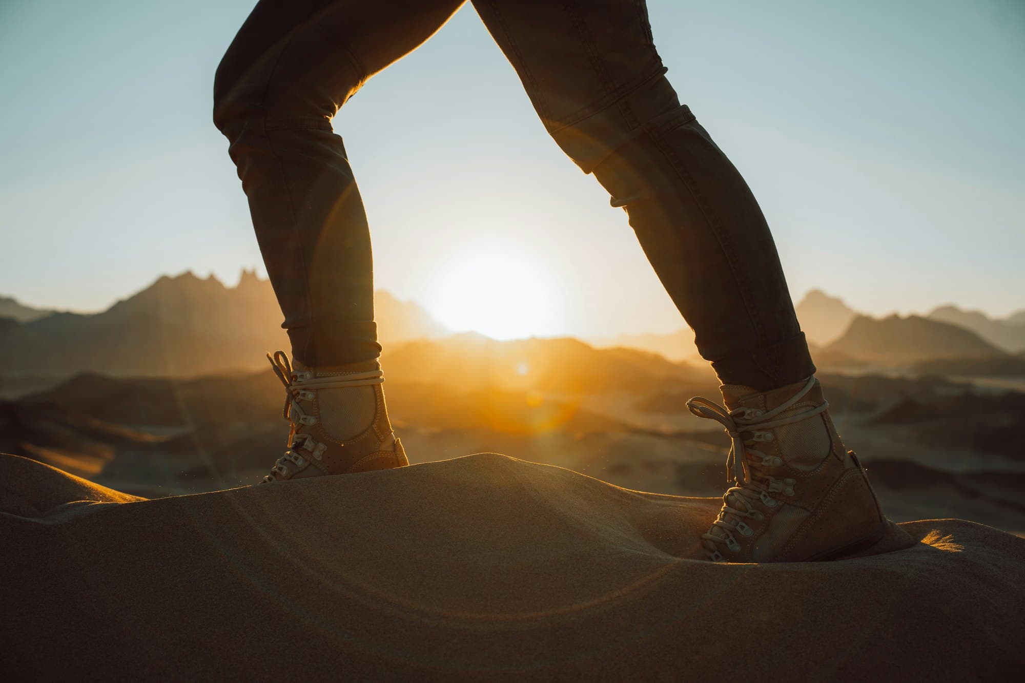 A person mid-stride on a sand dune, silhouetted against the sunrise
